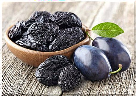 A bowl of prunes and two fresh plums.