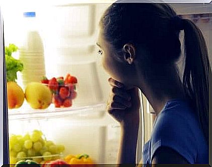 A woman looking at fruit and milk in the fridge at night.