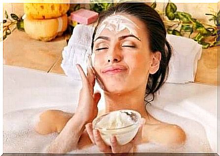 a woman applying a face mask in a bathtub